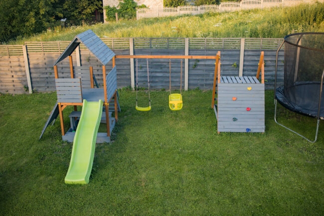 Drewniany domek dla dzieci zjeżdżalnią i drabinką w ogrodzie